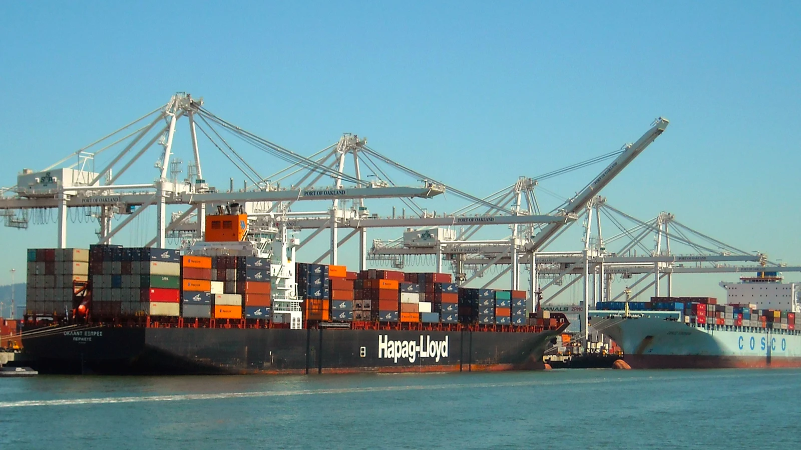 Loaded container ship under white gantry cranes at the Port of Oakland on a sunny day