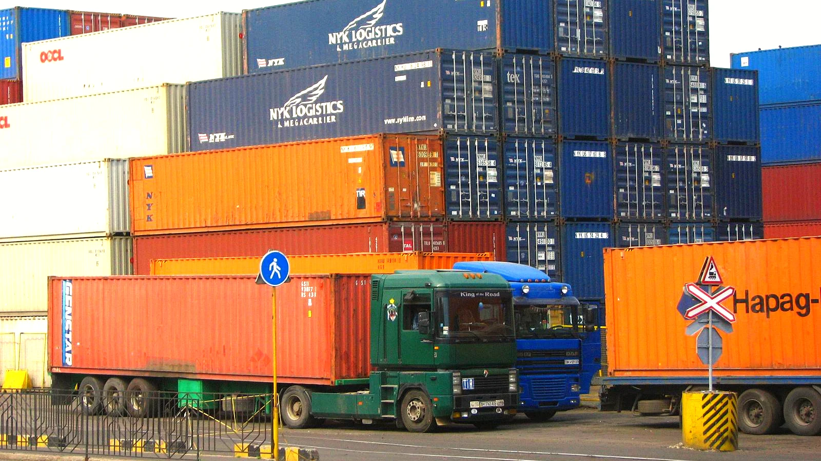 Trucks with containers parked among stacked colourful shipping containers in a port