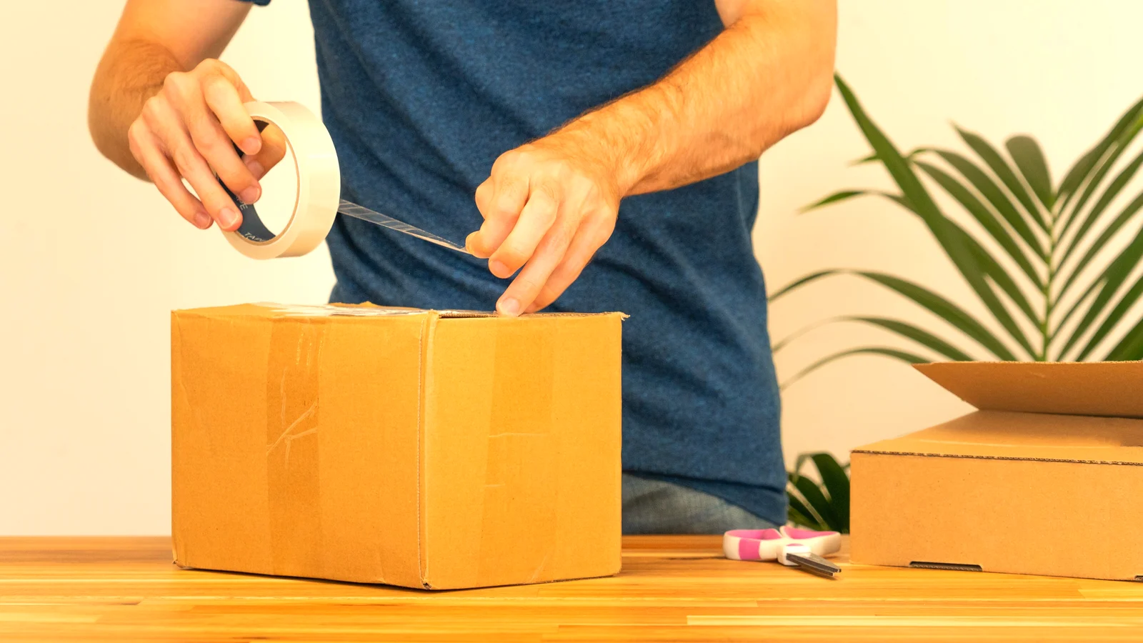 Person sealing a cardboard parcel with packing tape before shipping