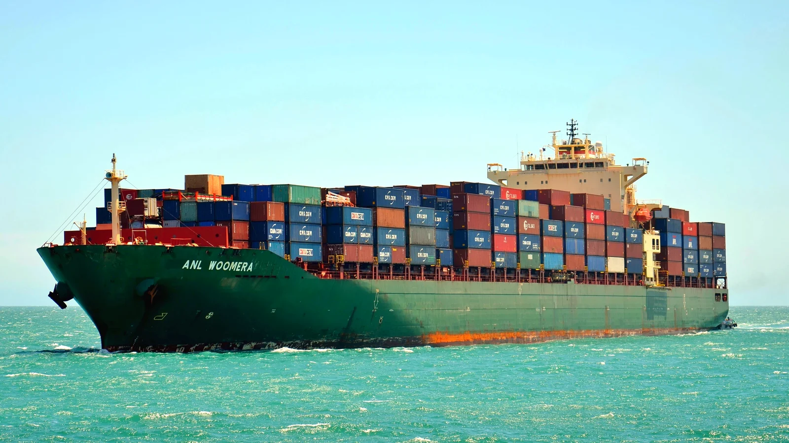 Fully laden container ship under way on turquoise water in clear daylight