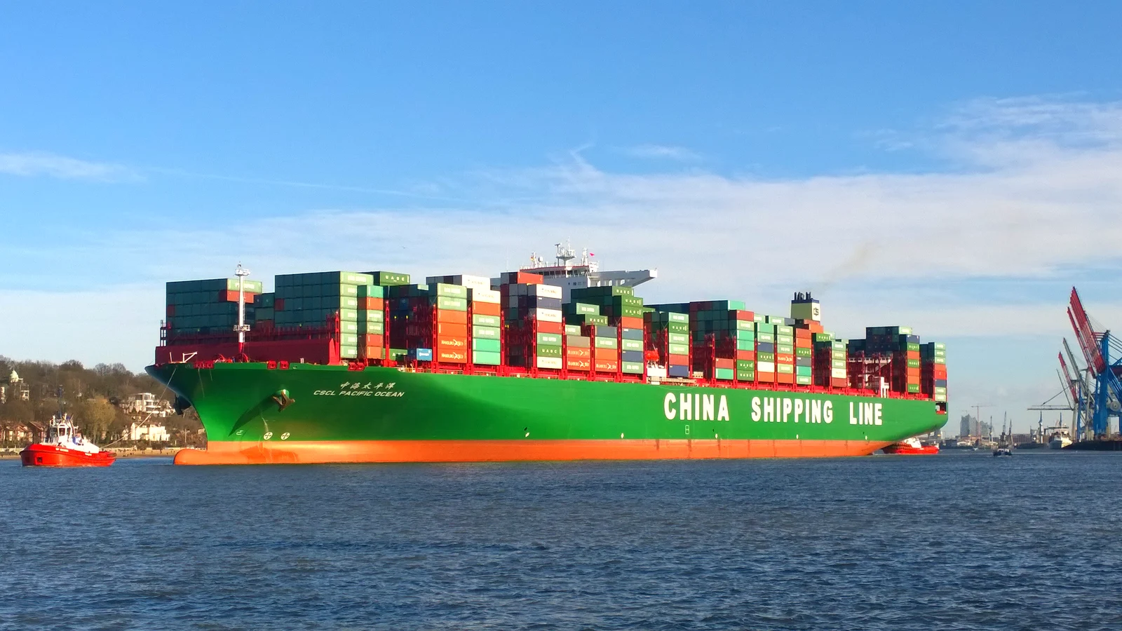 Container ship CSCL Pacific Ocean under a blue sky with a tug beside it