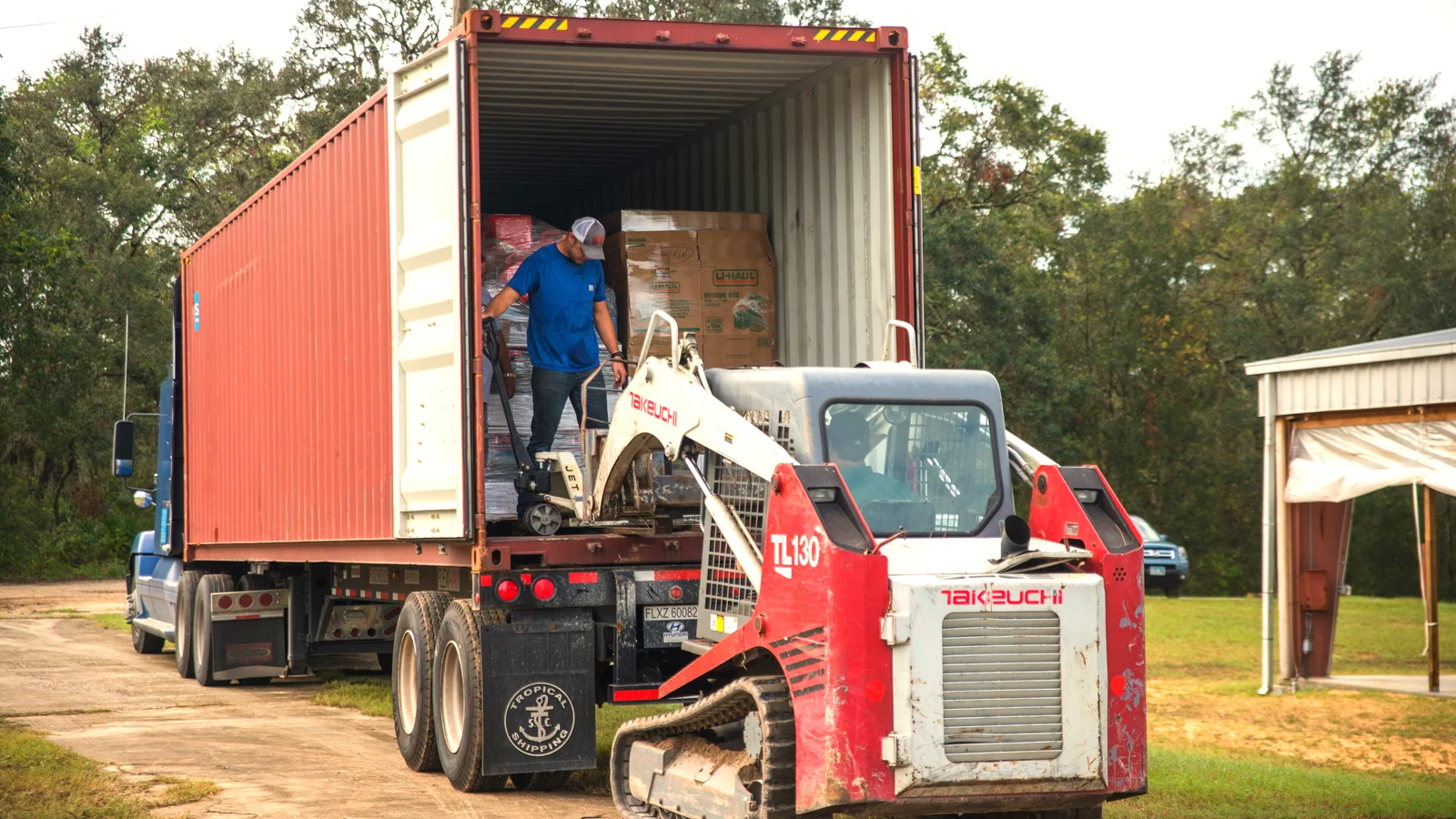Tracked loader moving cargo into an open red shipping container on a truck trailer