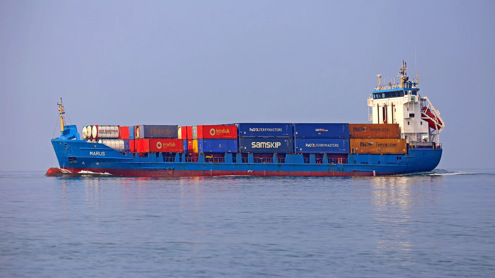 Feeder container ship Marus with stacked containers on calm water