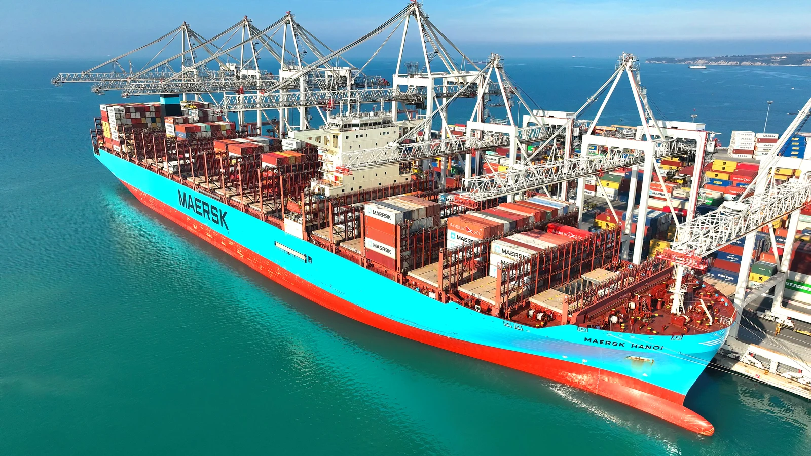 Aerial view of a blue Maersk container ship berthed beside gantry cranes in turquoise water